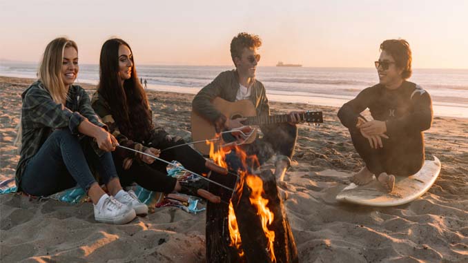 Four Young People Around A Fire At The Beach