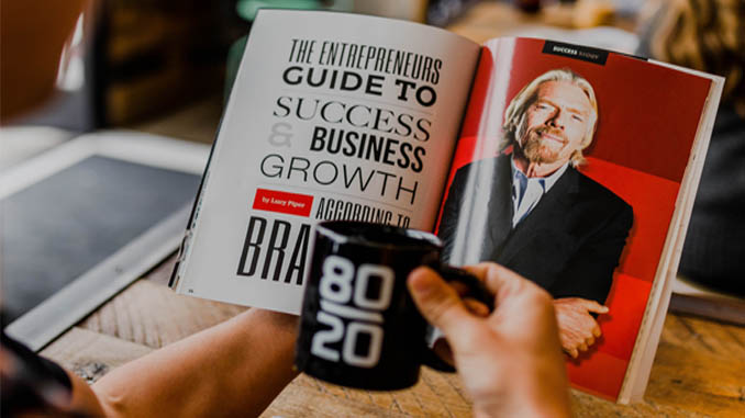 Man Holding Coffee Mug With "80/20" Reading A Success Book