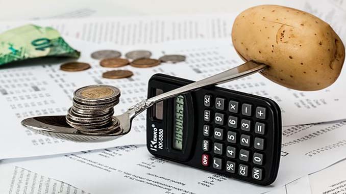 A Spoon Balancing On A Calculator With A Potato On One End And Coins On The Other