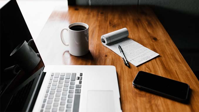 A Desk With A Laptop, Cellphone, Coffee And A Notepad
