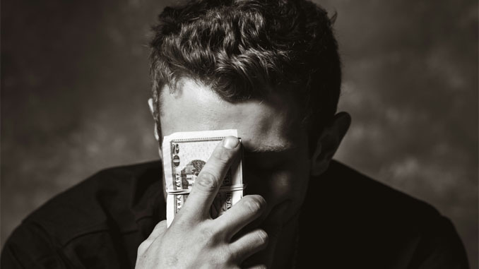 Man Holding A Stack Of Money To His Forehead