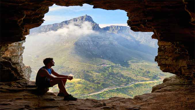 Man Sitting In A Cave Overlooking The Mountains
