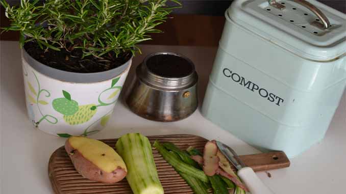 A Small Compost Bin On The Counter With Peeled Veggies