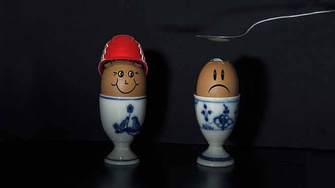 Two Eggs - One Wearing A Hard Hat One Not - Only One Is Cracked On Top