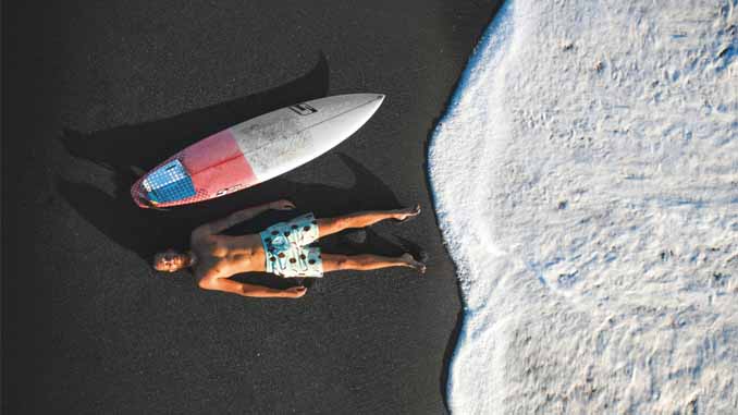 Man Laying On The Beach Beside His Board